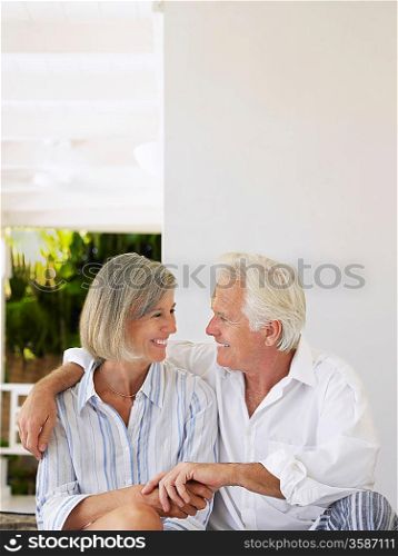 Senior couple sitting on verandah looking in eyes and smiling