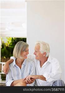 Senior couple sitting on verandah looking in eyes and smiling