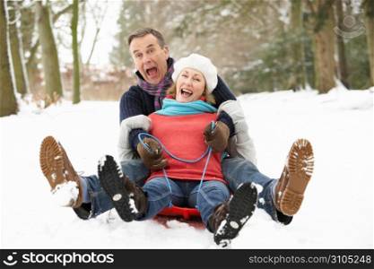 Senior Couple Sledging Through Snowy Woodland