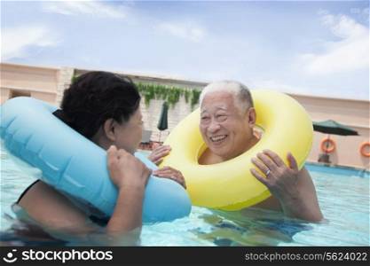 Senior couple smiling and relaxing in the pool with inflatable tubes