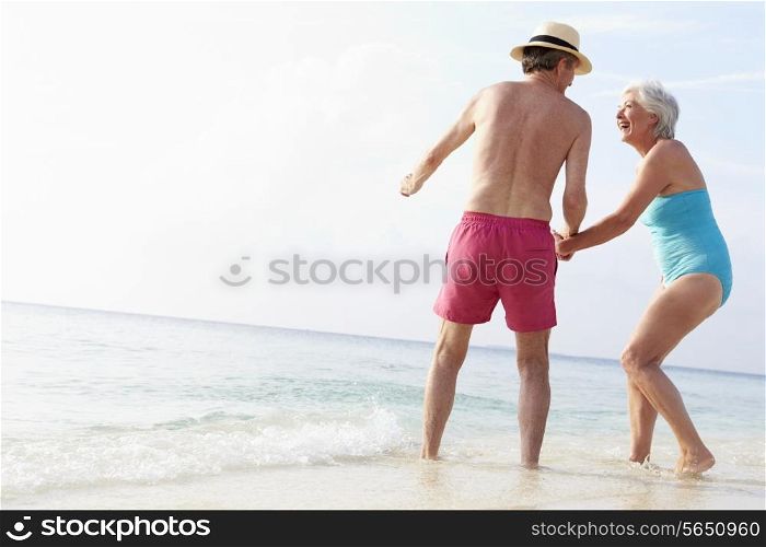 Senior Couple Splashing In Sea On Beach Holiday