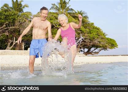 Senior Couple Splashing In Sea On Tropical Beach Holiday