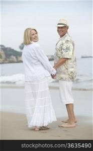 Senior couple stand holding hands on beach