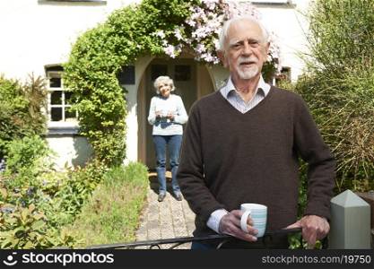 Senior Couple Standing In Cottage Garden Holding Coffee Cup