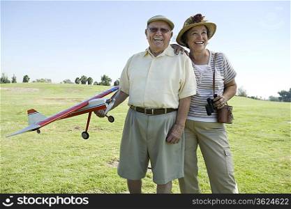 Senior couple standing on field, man holding model plane
