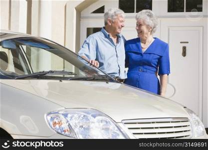 Senior couple standing with their car outside their home