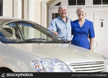 Senior couple standing with their car outside their home