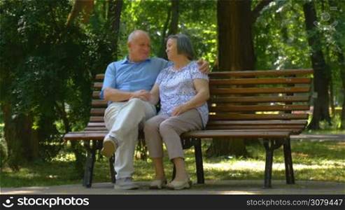 Senior couple talking while sitting on bench in summer park.