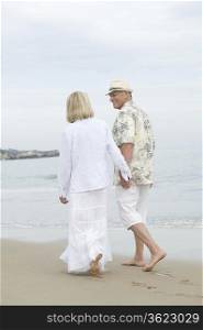 Senior couple walk holding hands on beach