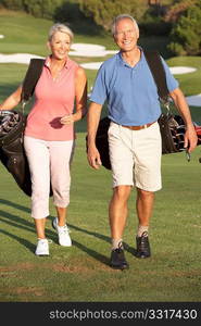 Senior Couple Walking Along Golf Course Carrying Bags