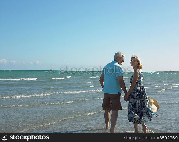 Senior couple walking on tropical beach back view