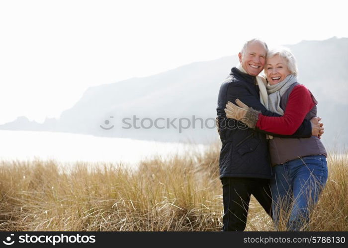 Senior Couple Walking Through Sand Dunes On Winter Beach