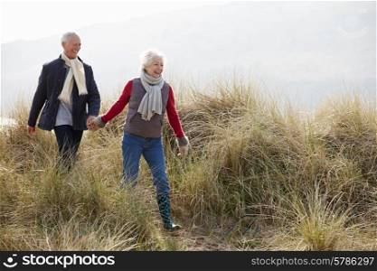 Senior Couple Walking Through Sand Dunes On Winter Beach