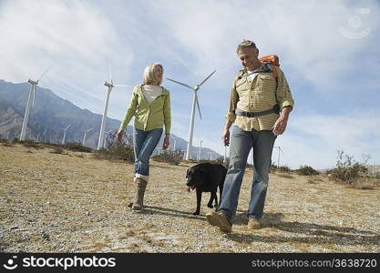 Senior couple walking with dog near wind farm