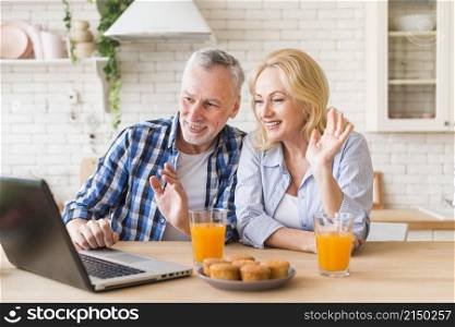 senior couple waving their hands during online video call laptop