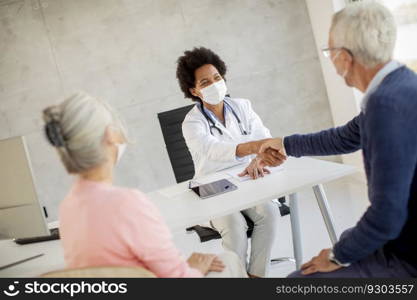 Senior couple with protective facial masks receive news from black female doctor in the office