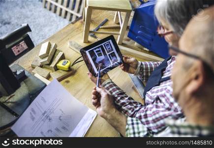 Senior couple working in a carpentry workshop looking tablet with chair design. Senior couple in a carpentry looking tablet