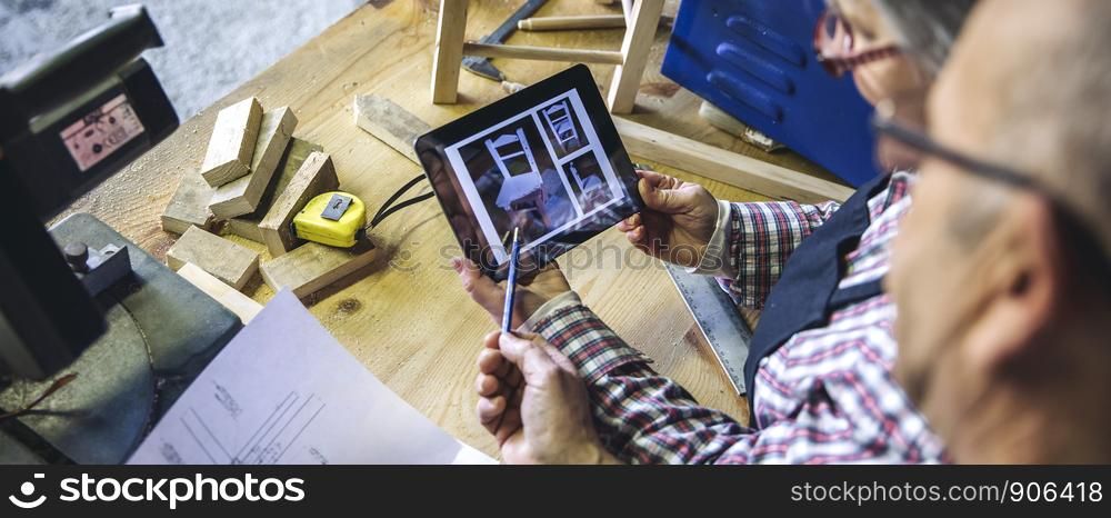 Senior couple working in a carpentry workshop looking tablet with chair design. Senior couple in a carpentry looking tablet