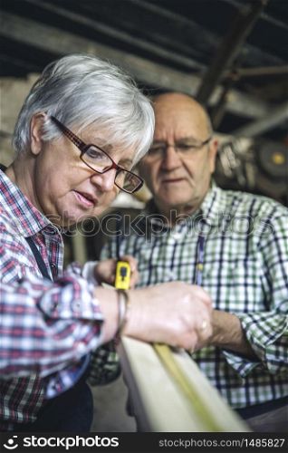Senior couple working in a carpentry workshop. Selective focus on woman in background. Senior couple in a carpentry