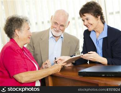 Senior couple working with a broker or advisor, signing paperwork.