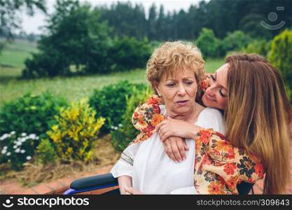 Senior dissatisfied woman in a wheelchair with her daughter in the garden. Senior dissatisfied woman in a wheelchair with her daughter
