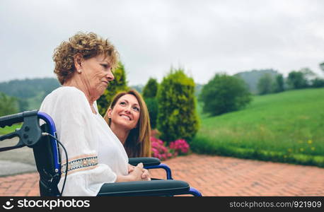 Senior dissatisfied woman in a wheelchair with her daughter in the garden. Senior dissatisfied woman in a wheelchair with her daughter