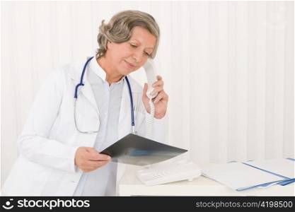 Senior doctor female on phone watch down x-ray at office