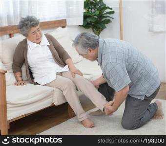 Senior elder asian man help his wife to sit on coach after fall down and get injury on leg or ankle in living at home.