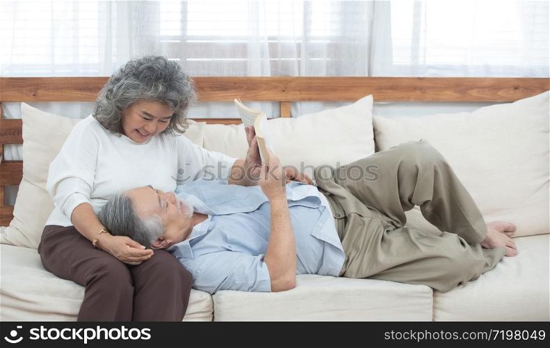 Senior elder asian man lie down on sofa read book with grandmother in living room at home.. elder couple sit on couch read book at home