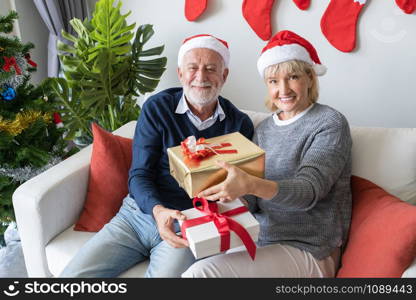 senior elderly caucasian old man and woman give gift presents to each other, they happy together in living room that decorated for christmas festival day in the morning, retirement lifestyle concept