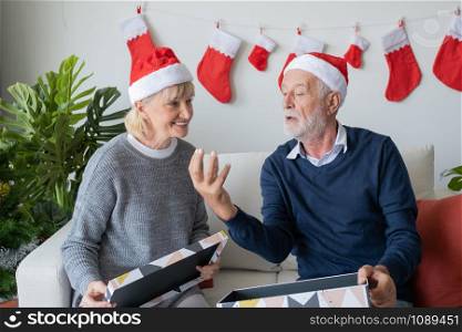 senior elderly caucasian old man and woman help open big gift presents box and happy together in living room that decorated with christmas tree for christmas festival day, lifestyle concept