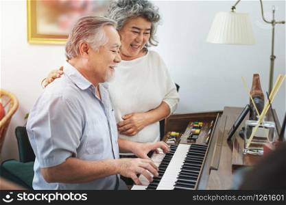 Senior elderly man plays piano in nursing home listened to by elderly woman,Retreatment elderly asian grandmother and grandfather play piano in home with love moment.