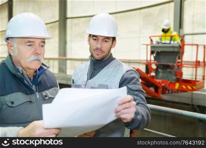 senior engineer and colleague in hardhat standing in factory