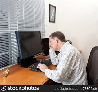 Senior executive in home office with two monitors and keyboard on leather desk and looking worried