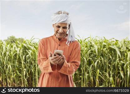 Senior farmer using mobile phone standing in field