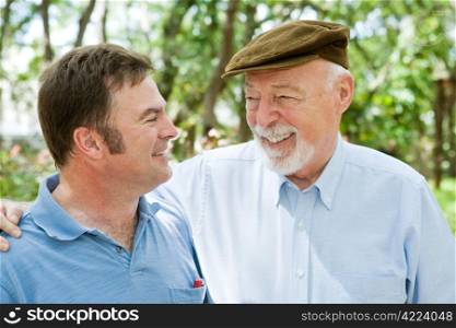 Senior father and adult son laughing together in the park.