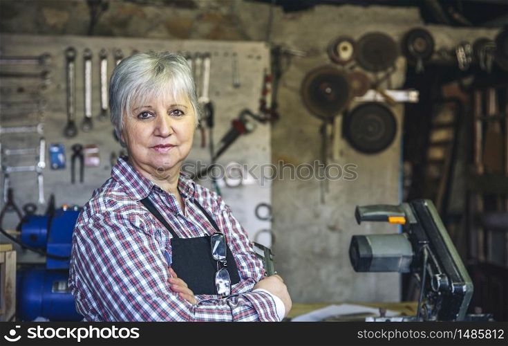 Senior female carpenter posing with crossed arms in his workshop. Female carpenter in his workshop