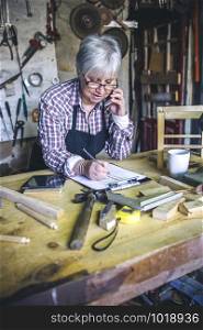 Senior female carpenter talking on the phone in his workshop. Female carpenter in his workshop