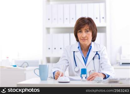 Senior female doctor sitting at desk working at offiice.