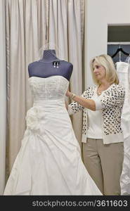 Senior female owner adjusting wedding dress on mannequin in bridal store