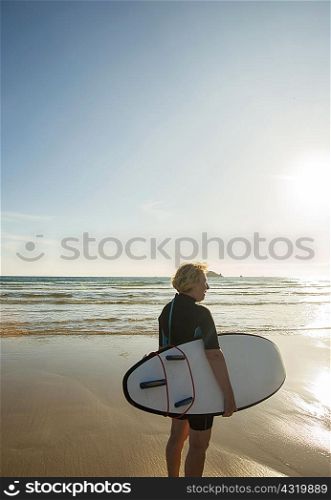Senior female surfer standing on beach with surfboard, Camaret-sur-mer, Brittany, France