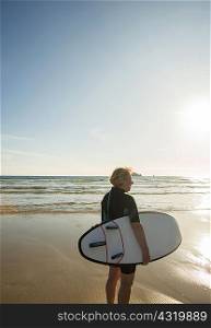 Senior female surfer standing on beach with surfboard, Camaret-sur-mer, Brittany, France