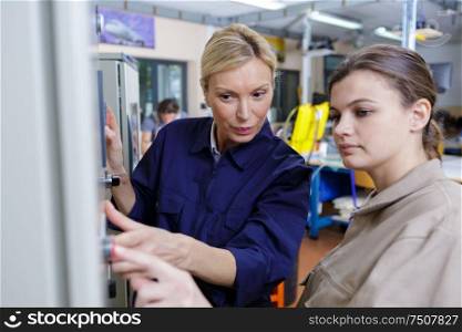 senior female worker training new recruit to use machine