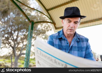 Senior gentleman reading newspaper in park. Enjoying reading