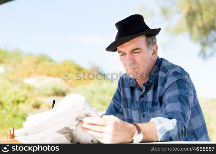 Senior gentleman reading newspaper in park. Enjoying reading