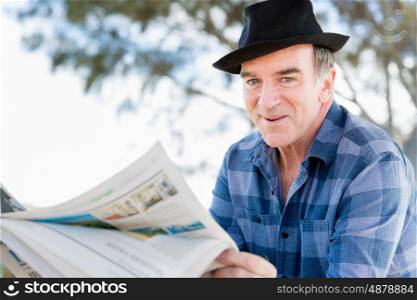 Senior gentleman reading newspaper in park. Enjoying reading