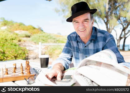 Senior gentleman reading newspaper in park. Enjoying reading