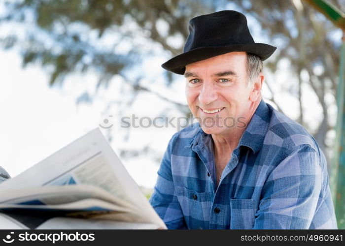 Senior gentleman reading newspaper in park. Enjoying reading