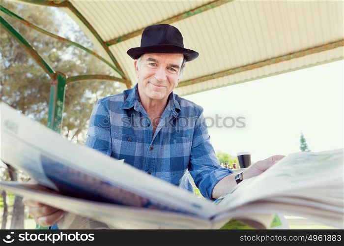 Senior gentleman reading newspaper in park. Enjoying reading
