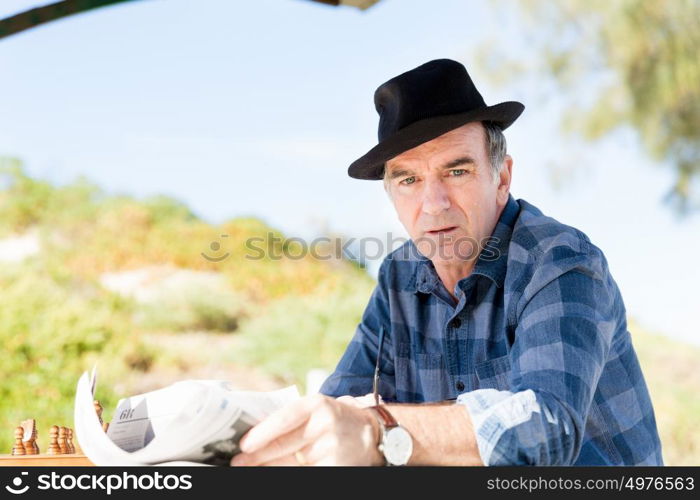 Senior gentleman reading newspaper in park. Enjoying reading